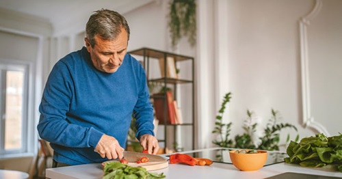 Mann kocht mit frischem Gemüse – herzgesunde Ernährung zur Vorbeugung von Folgen nach einem Herzinfarkt.