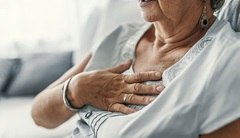 Frau mit Herzinfarkt, verursacht durch zu hohe Cholesterinwerte, hält sich die Hand an die Brust.